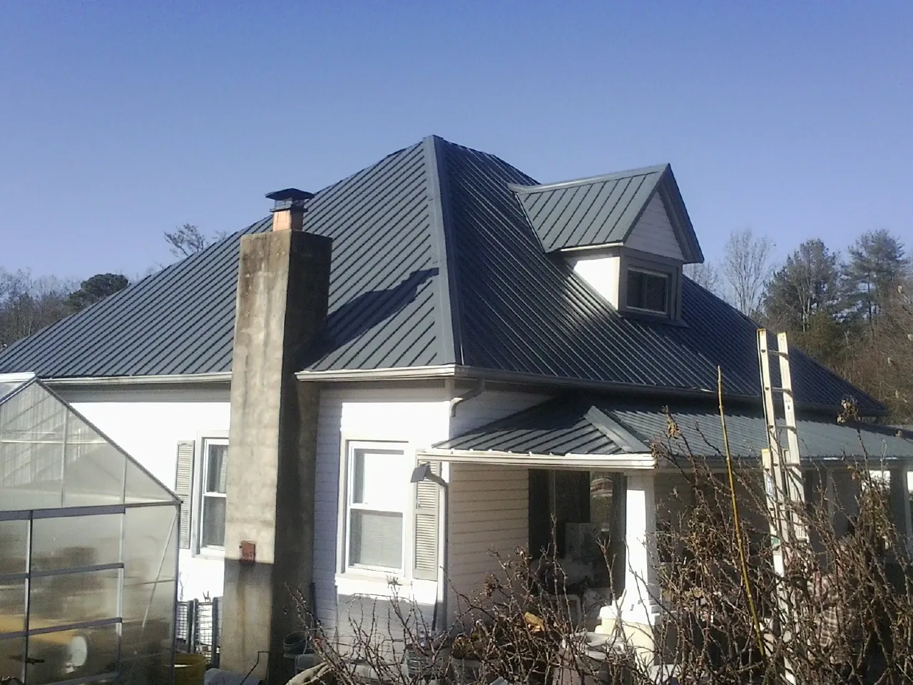 Dark blue standing seam metal roof on a white farmhouse with dormer — Slate & Tile Roof Repair by Roofing Brothers in New Madison