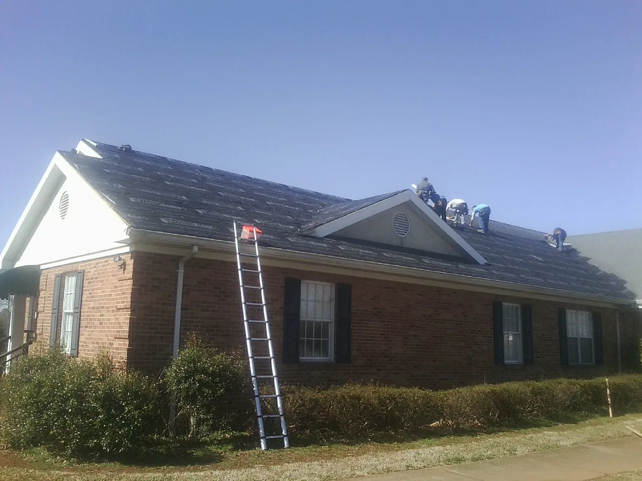 Crew tearing shingles off a brick ranch roof with a ladder set — Emergency Roof Repair work by our crew in New Madison