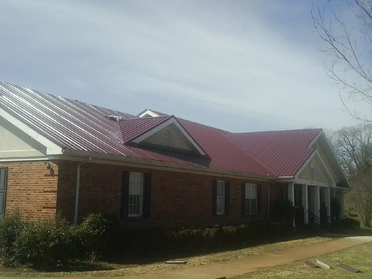 Red metal roof with gabled entries on a long brick building, from a Hail Damage Roof Repair job in New Madison