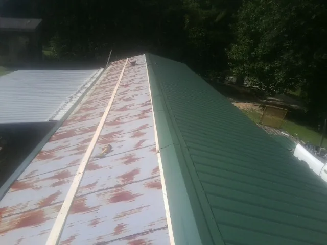 Old rusted panels beside newly installed green metal roofing — Wind Damage Roof Repair by Roofing Brothers in New Madison