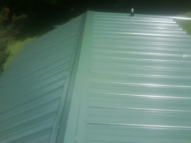 New green metal panels meeting at the ridge of a roof — Flat Roof Repair work by our crew in New Madison