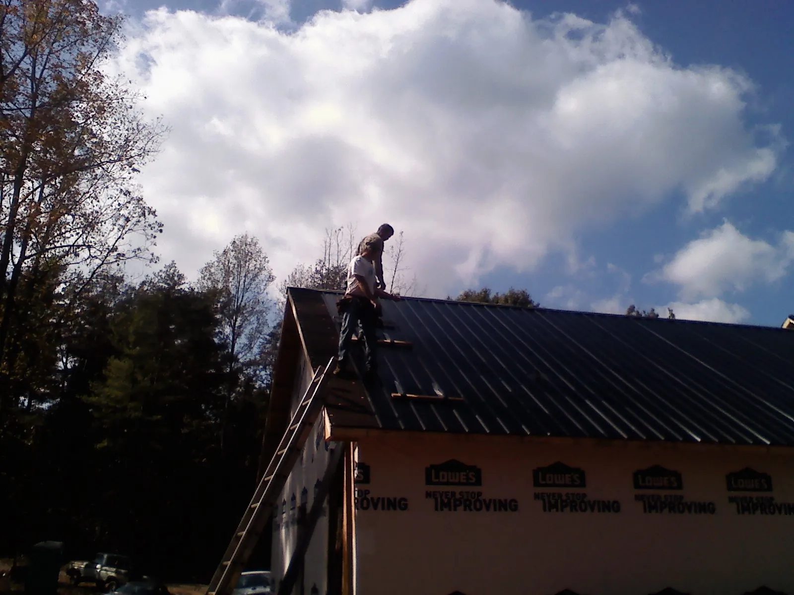 Roofer fastening dark metal panels high against a cloudy sky, from a Roof Inspection job in New Madison