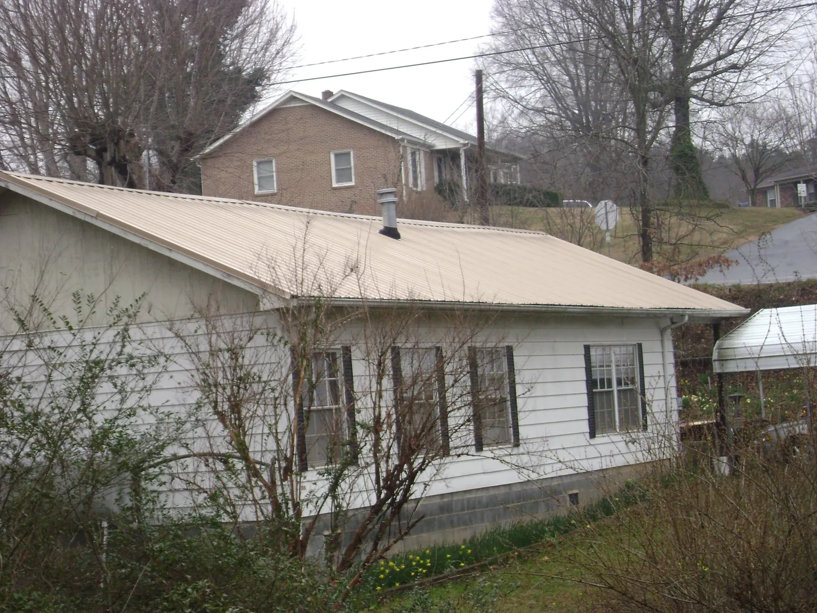 Tan metal roof on a white sided house set into a hillside — Commercial Roofing by Roofing Brothers in New Madison