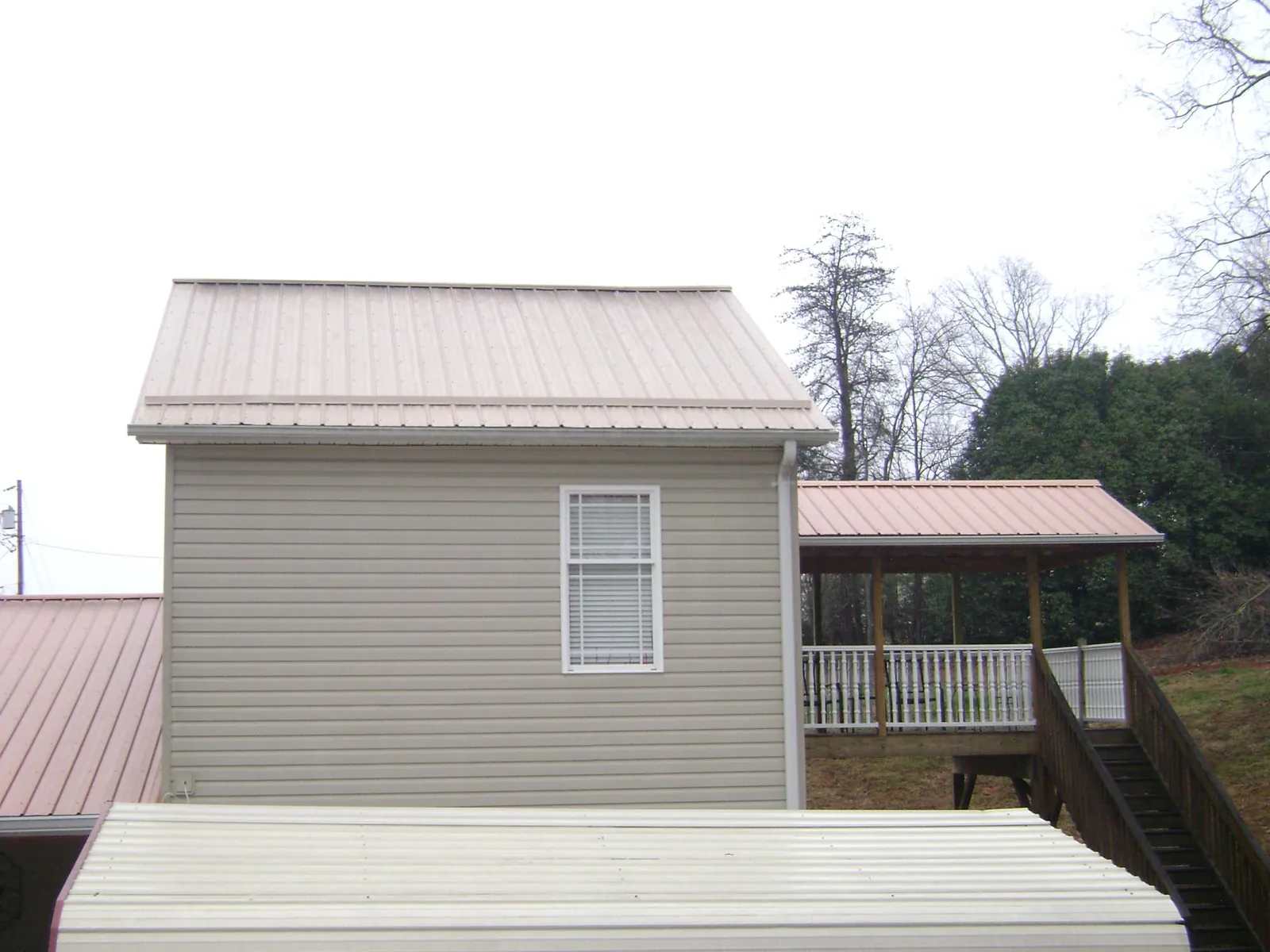 Tan metal roofs on a two story addition and attached porch, from a Roof Replacement job in New Madison